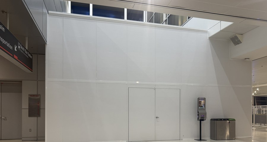 The finished 16 ft SwiftWall Pro barricade in the public concourse at Miami International Airport Terminal K, beside Baggage Claim signage